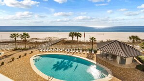 Ein Poolbereich mit Liegestühlen und einer überdachten Sitzgelegenheit mit Blick auf einen Strand und das Meer.