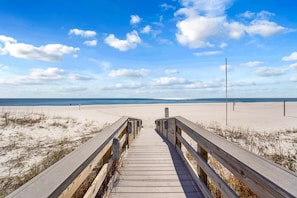 Une promenade en bois mène  à une plage de sable fin, sous un ciel dégagé.