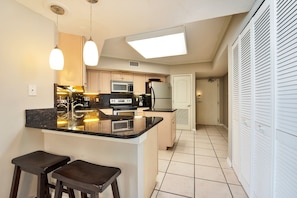 A modern kitchen with a central island, bar stools, a microwave, refrigerator, and a large window above the sink.