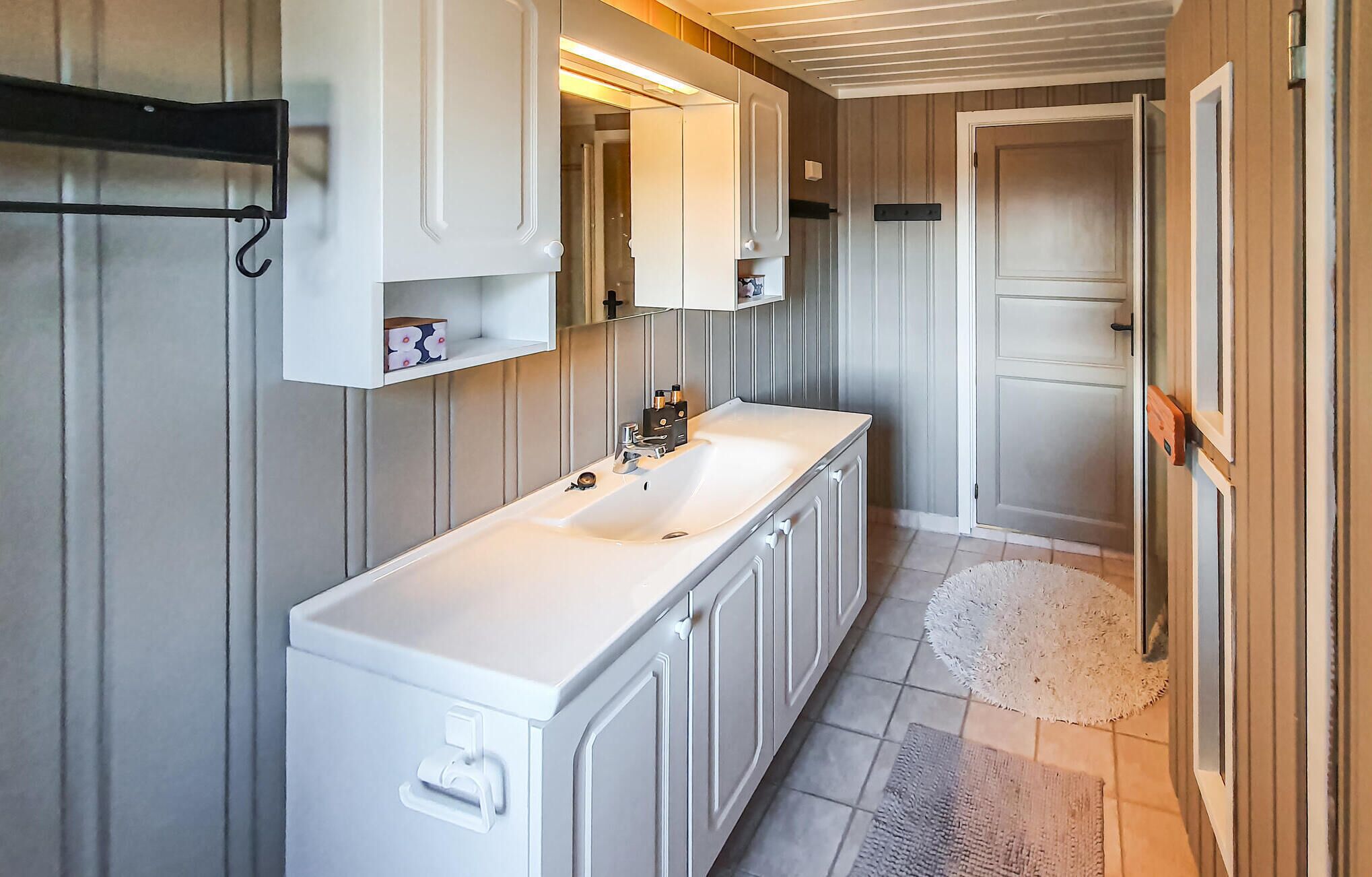 A narrow bathroom with a white sink, cabinets, and a mirror.