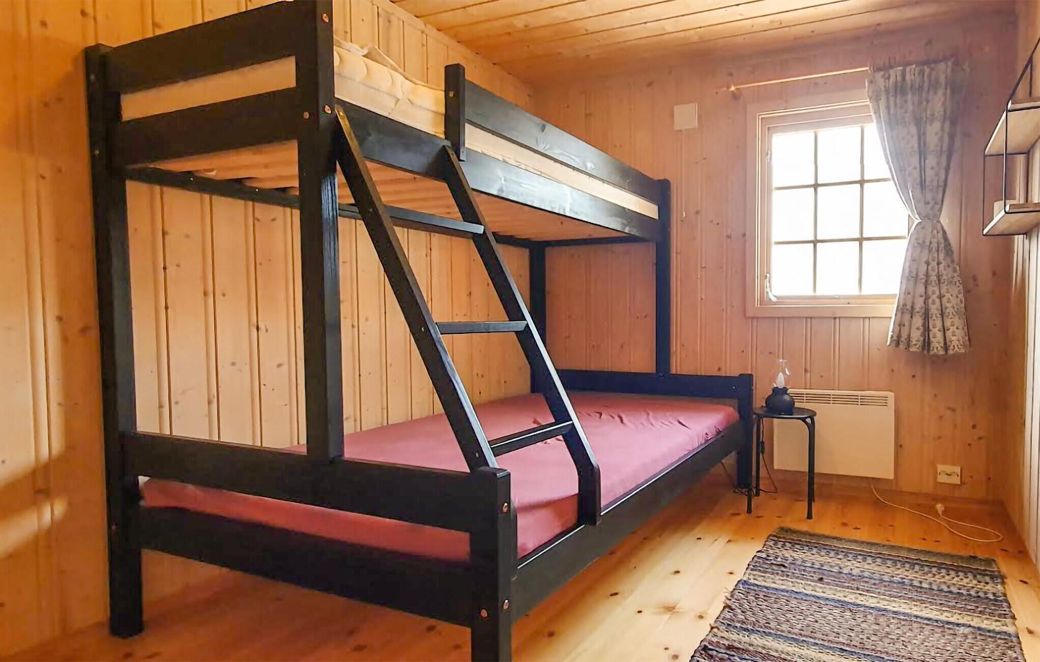 Un lit superposé avec une échelle, une petite table avec une lampe, une fenêtre avec des rideaux et un radiateur.