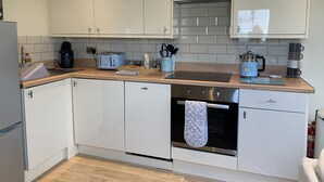 Eine moderne Küche mit weißen Schränken, einem Edelstahlbackofen, einer Kaffeemaschine und einem Wasserkocher auf der Arbeitsfläche.