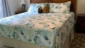 A bed with a tropical-themed bedspread, a wooden headboard, and a nightstand with a lamp and a vase. - Beautiful home in Kailua-Kona with easy access to all the Island. (KAILUA KONA)