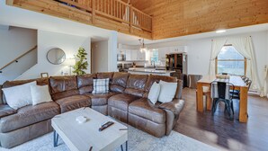 Een ruime woonkamer met een bruine leren zithoek, een houten eettafel met stoelen, en een keuken op de achtergrond.