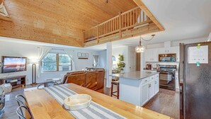 Een ruime keuken met een centraal eiland, houten plafond en een eethoek met een gestreepte tafelkleed.