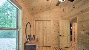 Una habitación de cabaña de madera con un ventanal grande, un espejo, una mesa y una cama.