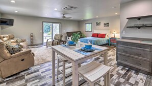 A modern living room with a sofa, a dining table, and a kitchen area with a dresser and shelves. - Detached Watauga Riverfront Studio w/ Grill (Elizabethton)