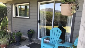 A patio with a blue chair and table, potted plants, and a sliding glass door. - Spacious one bedroom suite (Campbell River)