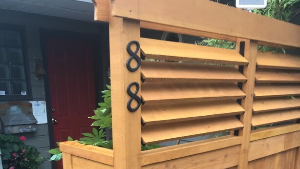 A wooden fence with the number 8, a potted plant, and a red door in the background. - Spacious one bedroom suite (Campbell River)