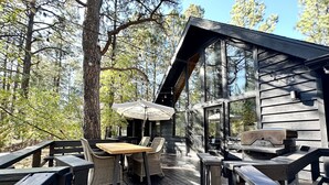Eine Terrasse im Freien mit Holzmöbeln, darunter ein Tisch, Stühle und ein Grill.