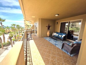 A balcony with a sofa and chairs, a potted plant, and a view of palm trees and buildings.