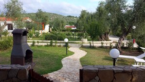 A stone pathway leading through a garden with a rustic stone structure, a red-roofed building, and a hill in the background. - Bungalow with pool and barbecue (Vieste)