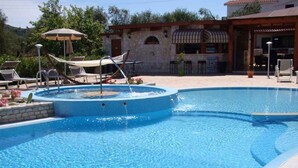 A swimming pool with lounge chairs and umbrellas, a stone building with a tiled roof, and a clear blue sky. - Bungalow with pool and barbecue (Vieste)