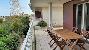 Un balcón con una mesa y sillas de madera, una planta en maceta y vistas de una noria.