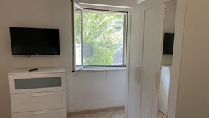 Ein Zimmer mit einem großen Fenster, einem an der Wand befestigten Flachbildfernseher und einer weißen Kommode mit Schubladen.