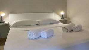 Una cama bien hecha con sábanas blancas, dos lámparas de noche y toallas enrolladas sobre la cama.