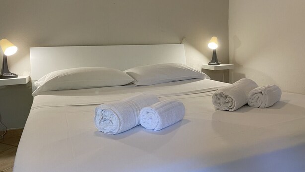 Ein ordentlich bezogenes Bett mit weißen Leinentüchern, zwei Nachttischlampen und zusammengerollten Handtüchern.