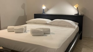 En snyggt bäddad säng med vita lakan och handdukar, en mörk sänggavel och två sänglampor.