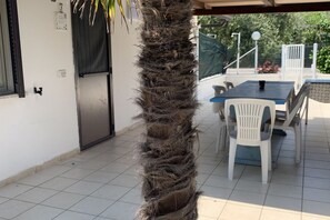 A covered patio area with a tiled floor, a table with chairs, and a palm tree.