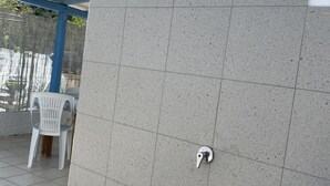 Un muro rivestito di piastrelle, con un rubinetto e una sedia di plastica bianca.