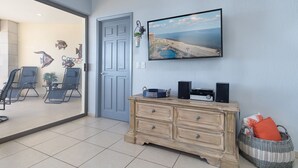 Ein Wohnzimmer mit einem großen Fernseher, einer Holzkommode und einem Korbwäschesammler.