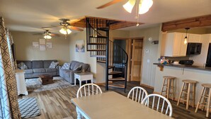 A spacious living room with a gray sofa, a dining table with white chairs, and a wooden staircase leading to a loft. - Private beach location (Oscoda)
