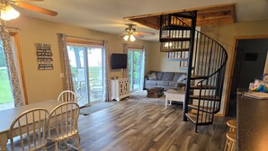 A spacious living area with a wooden floor, a dining table with chairs, a sofa, a TV, and a spiral staircase. - Private beach location (Oscoda)