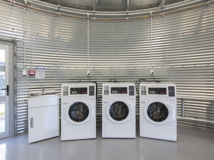 A laundry facility with three stacked washing machines, a metal wall, and a door leading outside.