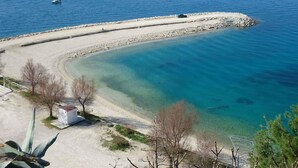 Uma área costeira com uma praia arenosa curvilínea, águas azuis cristalinas e um pequeno barco à distância.