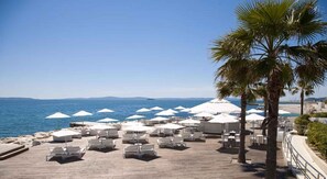 A beachside patio with white umbrellas and lounge chairs, overlooking the sea. - Holiday Apartment Samo 100 m from the Adriatic (Split)