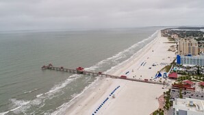 A beach with a pier, beach umbrellas, and a large hotel.