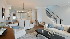 A spacious living room with a large sofa, a coffee table, and a dining area with a chandelier.
