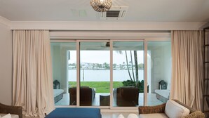 A modern living room with a large sliding glass door leading to an outdoor area with a view of the water and greenery.