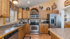 Una cocina con armarios de madera, microondas, estufa, refrigerador y un lavamanos.