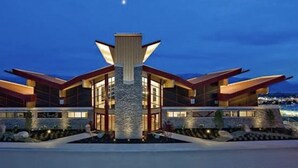 A modern building with a central tower and multiple wings, featuring large windows and a stone facade. - Pools open May long weekend!  Holiday Time @ West Kelowna's hidden gem!  2BR (West Kelowna)