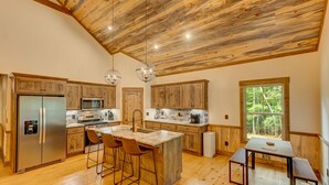 Cucina spaziosa con mobili in legno, un'isola centrale con sgabelli, una grande finestra e un soffitto alto con travi a vista.
