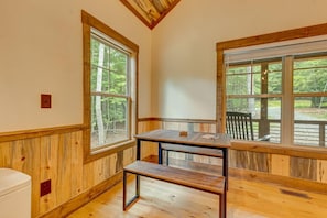 Ein Zimmer mit Holzwänden und -böden, großen Fenstern mit Blick auf Bäume, einer Holzbank und einem kleinen Tisch.