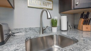 Una cocina con un lavamanos de acero inoxidable, encimera de mármol, una planta en maceta y un bloque de cuchillos.