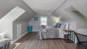 Un dormitorio con techo estilo loft, una cama con manta estampada, una mesita de noche y un ventanal con persianas.