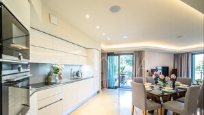 A modern kitchen with white cabinets, a built-in oven, and a dining area with a glass table and grey chairs. - Parc Du Cap 2 bedroom apartment VRBO (Antibes)
