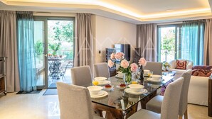 A modern dining area with a glass table, chairs, and a view of the outdoors. - Parc Du Cap 2 bedroom apartment VRBO (Antibes)