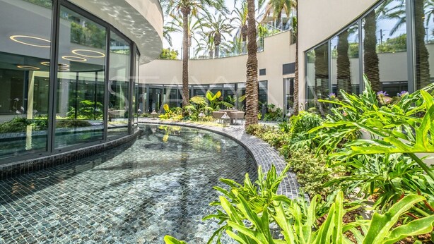 A modern building with a glass facade, a circular pool, and tropical landscaping. - Parc Du Cap 2 bedroom apartment VRBO (Antibes)