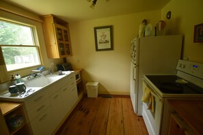 A kitchen with wooden floors, white cabinets, a refrigerator, and a stove.