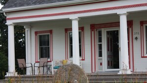 A white building with red trim and columns, numbered 376, featuring a porch with chairs and a large rock in the foreground. - Relax at the historic Austin House (Addison)