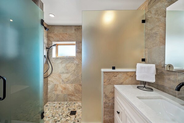 A modern bathroom with a glass shower enclosure, a built-in window, a white vanity, and a large mirror.