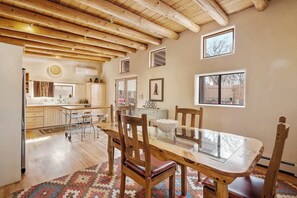 A spacious kitchen with wooden beams, a dining area with a glass table, and a view of the backyard through windows.