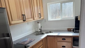 Una cocina con armarios de madera, un refrigerador de acero inoxidable, una estufa empotrada, un lavamanos y una ventana.