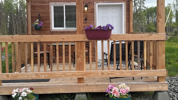Una cabaña de madera con un porche, dos ventanas, una puerta y dos macetas con flores.