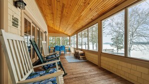 A covered porch with wooden flooring and large windows offering a view of a snowy landscape. - Bishop | Amazing location on Rangeley Lake and close to downtown (Rangeley)