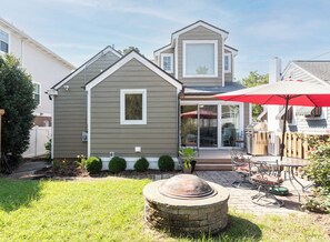 Ein zweistöckiges Haus mit einer Terrasse, die einen Grill, Gartenmöbel und einen roten Sonnenschirm zeigt.
